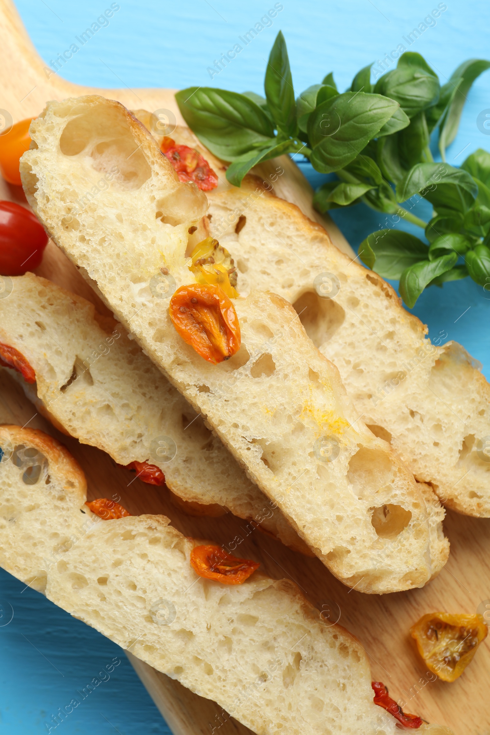 Pieces of delicious focaccia with tomatoes and basil on light blue table, flat lay Photo of Pieces of delicious focaccia with tomatoes and basil on light blue table, flat lay