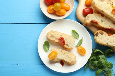 Photo of Pieces of delicious focaccia with tomatoes and basil on light blue wooden table, flat lay. Space for text