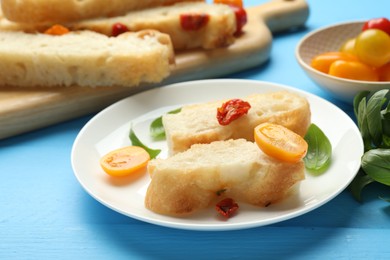 Photo of Pieces of delicious focaccia with tomatoes and basil on light blue wooden table, closeup