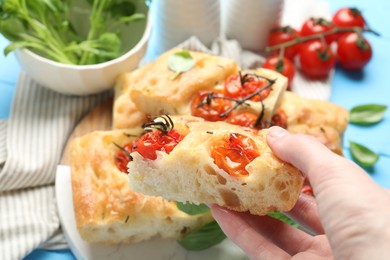 Photo of Woman holding piece of delicious focaccia with tomatoes at table, closeup