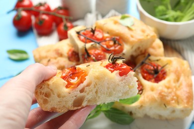 Photo of Woman holding piece of delicious focaccia with tomatoes at table, closeup
