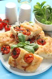 Photo of Pieces of delicious focaccia with tomatoes and basil on light blue wooden table, closeup