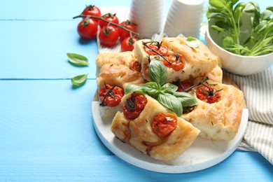 Photo of Pieces of delicious focaccia with tomatoes and basil on light blue wooden table, closeup