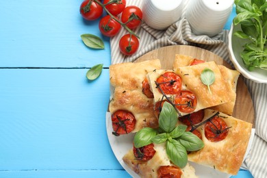 Photo of Pieces of delicious focaccia with tomatoes and spices on light blue wooden table, flat lay. Space for text