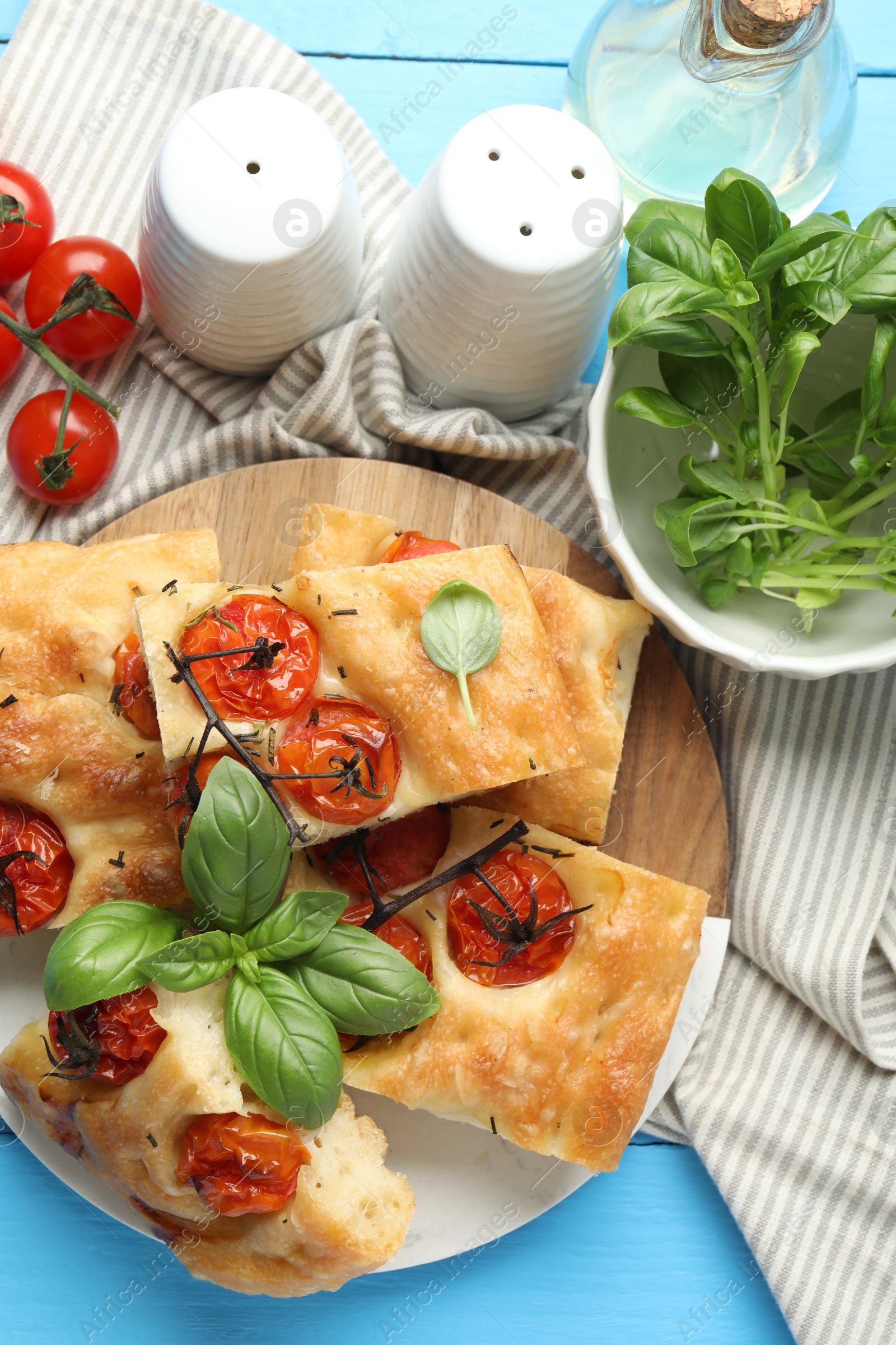 Pieces of delicious focaccia with tomatoes, spices and oil on light blue wooden table, flat lay Photo of Pieces of delicious focaccia with tomatoes, spices and oil on light blue wooden table, flat lay