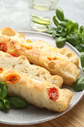 Photo of Pieces of delicious focaccia with tomatoes, basil and glass of water on gray table, closeup