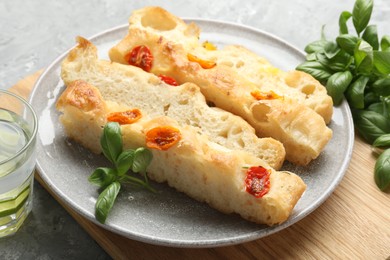 Photo of Pieces of delicious focaccia with tomatoes and basil on gray table, closeup