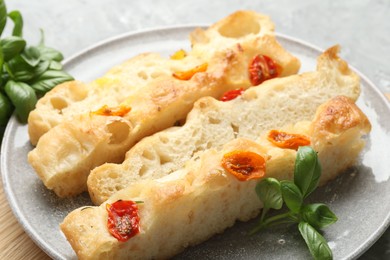 Photo of Pieces of delicious focaccia with tomatoes and basil on gray table, closeup