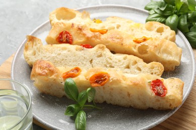 Photo of Pieces of delicious focaccia with tomatoes and basil on gray table, closeup
