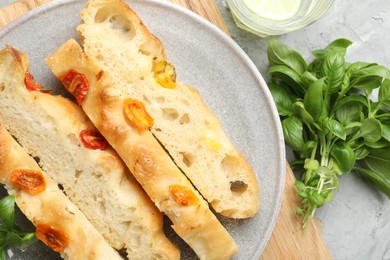 Photo of Pieces of delicious focaccia with tomatoes and basil on gray textured table, flat lay