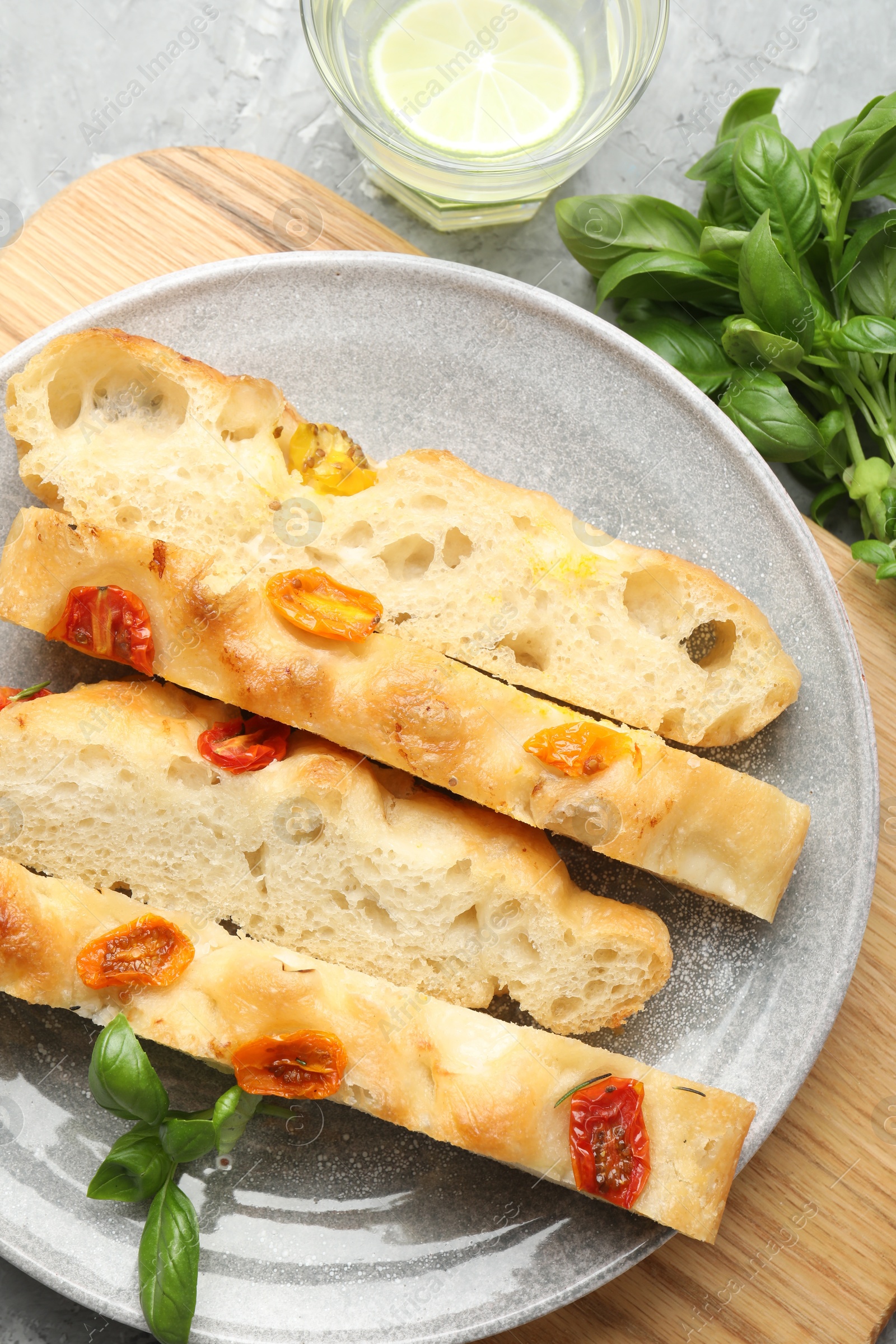 Pieces of delicious focaccia with tomatoes, basil and glass of water on gray textured table, flat lay Photo of Pieces of delicious focaccia with tomatoes, basil and glass of water on gray textured table, flat lay