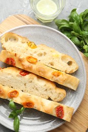 Photo of Pieces of delicious focaccia with tomatoes, basil and glass of water on gray textured table, flat lay