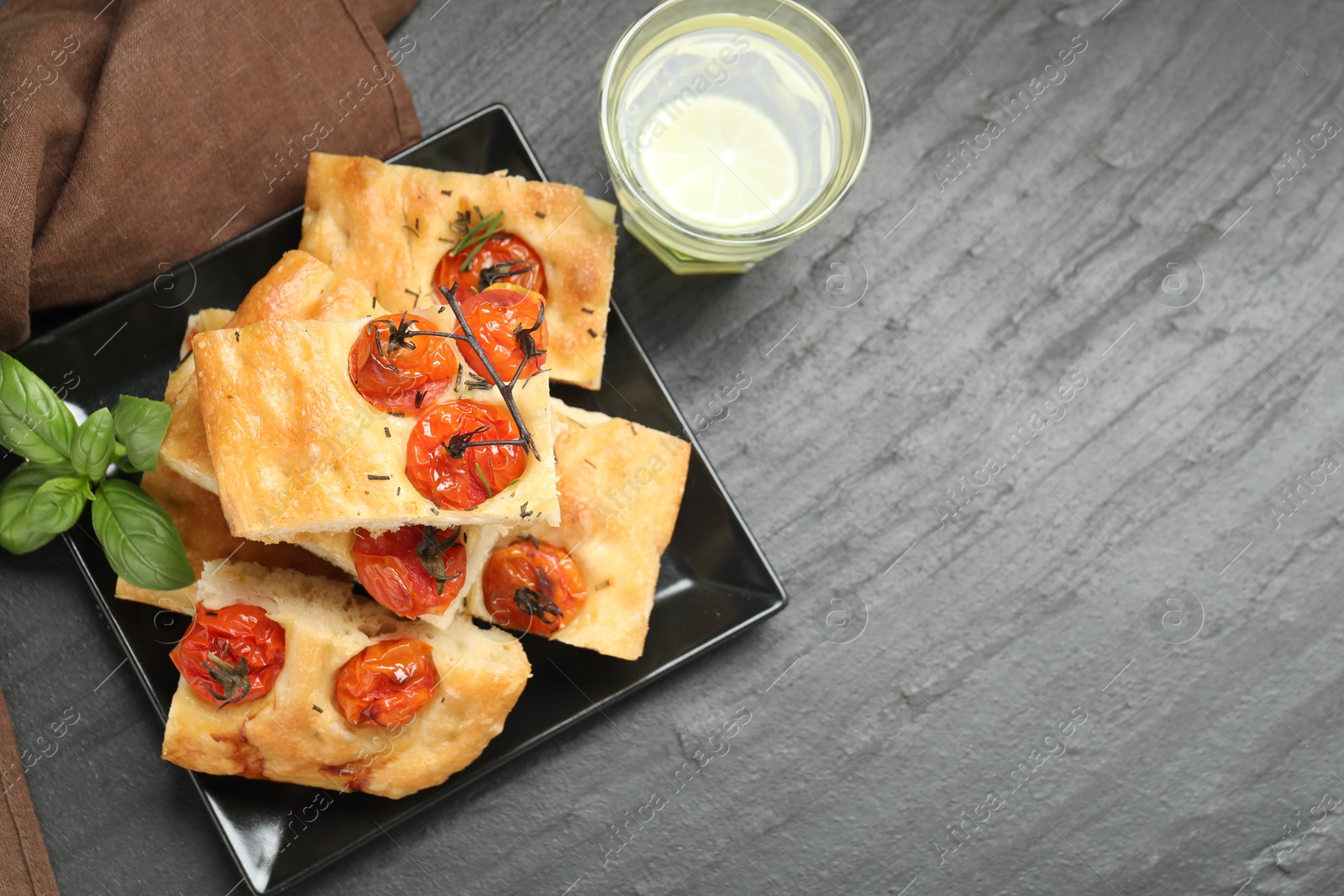 Pieces of delicious focaccia with tomatoes, spices and glass of water on gray textured table, flat lay. Space for text Photo of Pieces of delicious focaccia with tomatoes, spices and glass of water on gray textured table, flat lay. Space for text