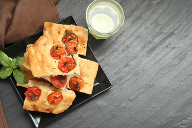 Photo of Pieces of delicious focaccia with tomatoes, spices and glass of water on gray textured table, flat lay. Space for text