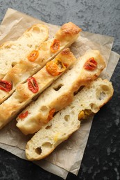 Photo of Pieces of delicious focaccia with tomatoes on dark textured table, top view