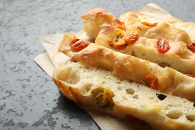 Photo of Pieces of delicious focaccia with tomatoes on gray textured table, closeup