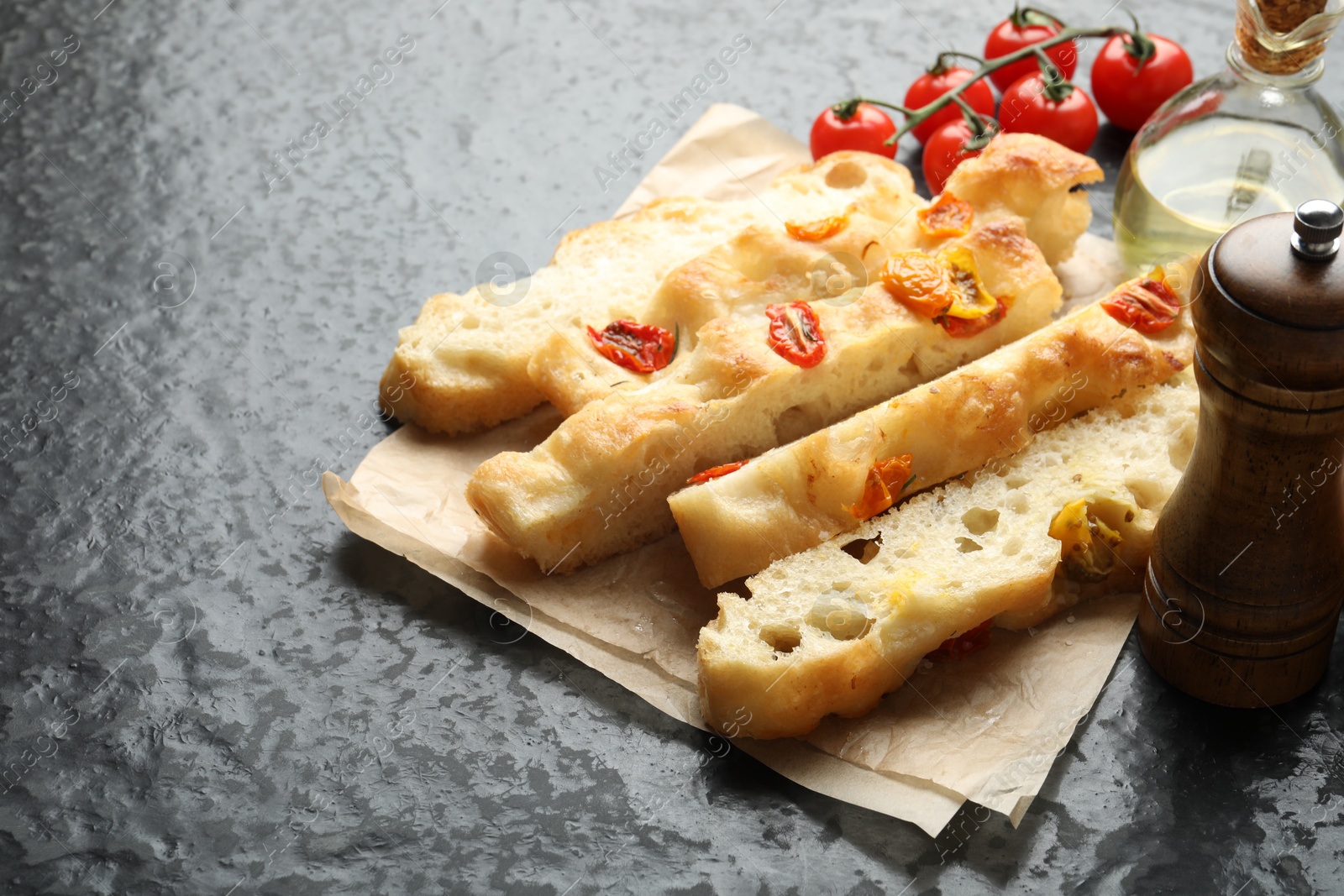 Pieces of delicious focaccia with tomatoes, spices and oil on gray textured table, closeup Photo of Pieces of delicious focaccia with tomatoes, spices and oil on gray textured table, closeup