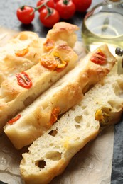 Photo of Pieces of delicious focaccia with tomatoes and oil on table, closeup