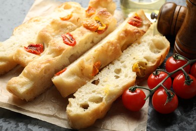 Photo of Pieces of delicious focaccia with tomatoes, spices and oil on table, closeup