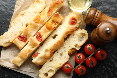 Photo of Pieces of delicious focaccia with tomatoes, spices and oil on dark table, flat lay