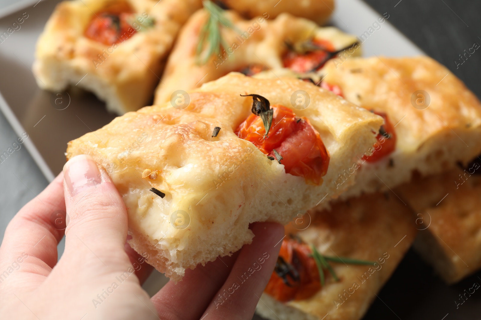 Woman holding piece of delicious focaccia with tomatoes and spices at table, closeup Photo of Woman holding piece of delicious focaccia with tomatoes and spices at table, closeup