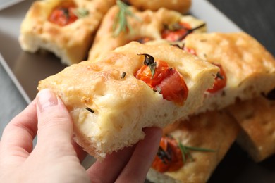 Photo of Woman holding piece of delicious focaccia with tomatoes and spices at table, closeup