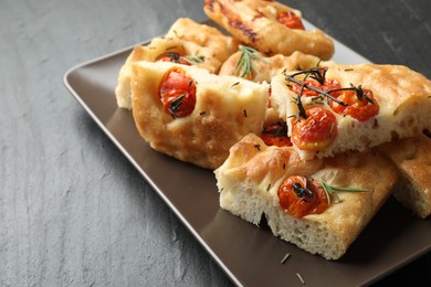 Photo of Pieces of delicious focaccia with tomatoes and spices on gray textured table, closeup