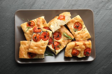 Photo of Pieces of delicious focaccia with tomatoes and spices on gray textured table, top view