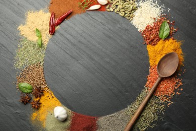 Photo of Different aromatic spices and spoon on dark textured table, top view. Space for text