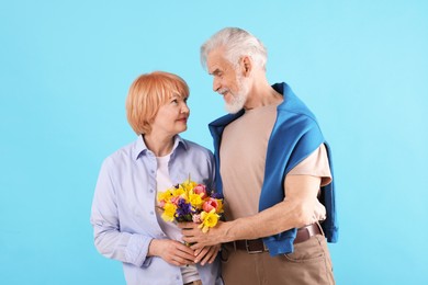 Photo of Lovely senior couple with bouquet of flowers on light blue background