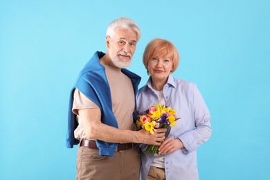Photo of Lovely senior couple with bouquet of flowers on light blue background