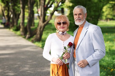 Photo of Lovely senior couple with rose in park, space for text