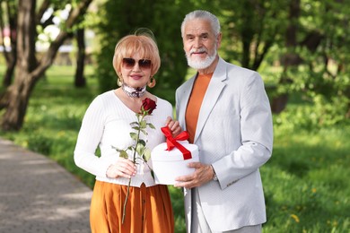Photo of Lovely senior couple with gift box and rose in park