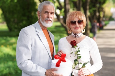 Photo of Lovely senior couple with gift box and rose in park