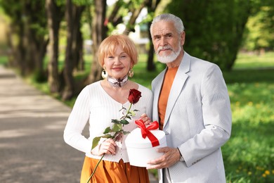 Photo of Lovely senior couple with gift box and rose in park