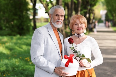 Photo of Lovely senior couple with gift box and rose in park