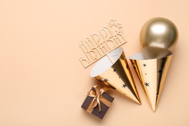 Photo of Party hats, topper, gift box and balloon on beige background, flat lay. Space for text