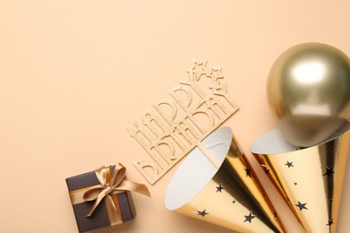 Photo of Party hats, topper, gift box and balloon on beige background, flat lay. Space for text