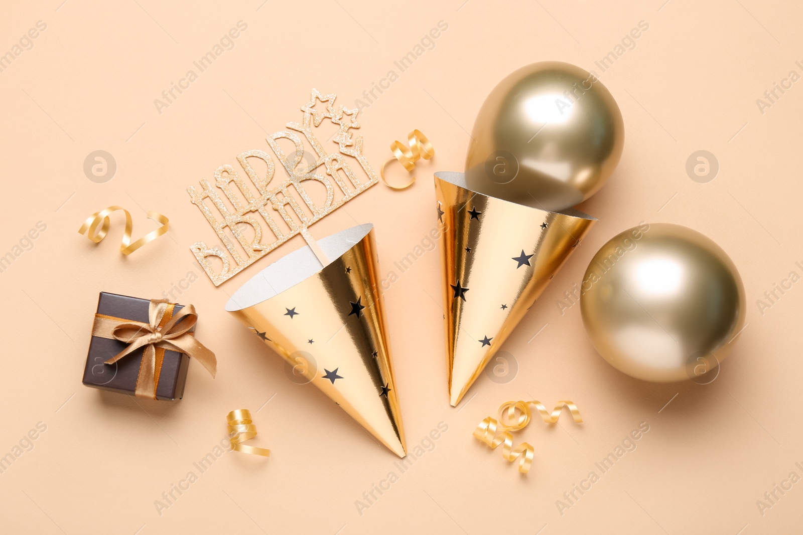Party hats, topper, gift box and balloons on beige background, flat lay Photo of Party hats, topper, gift box and balloons on beige background, flat lay