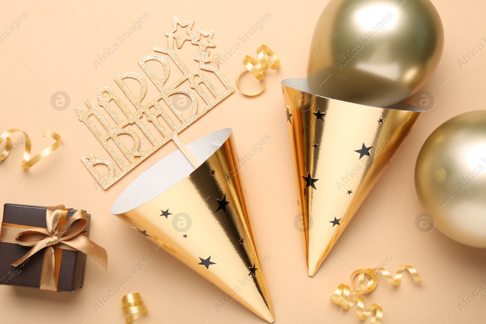 Party hats, topper, gift box and balloons on beige background, flat lay Photo of Party hats, topper, gift box and balloons on beige background, flat lay