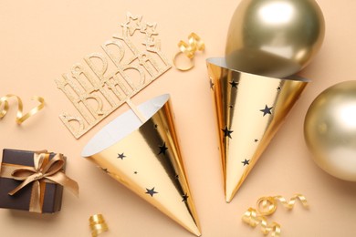 Photo of Party hats, topper, gift box and balloons on beige background, flat lay