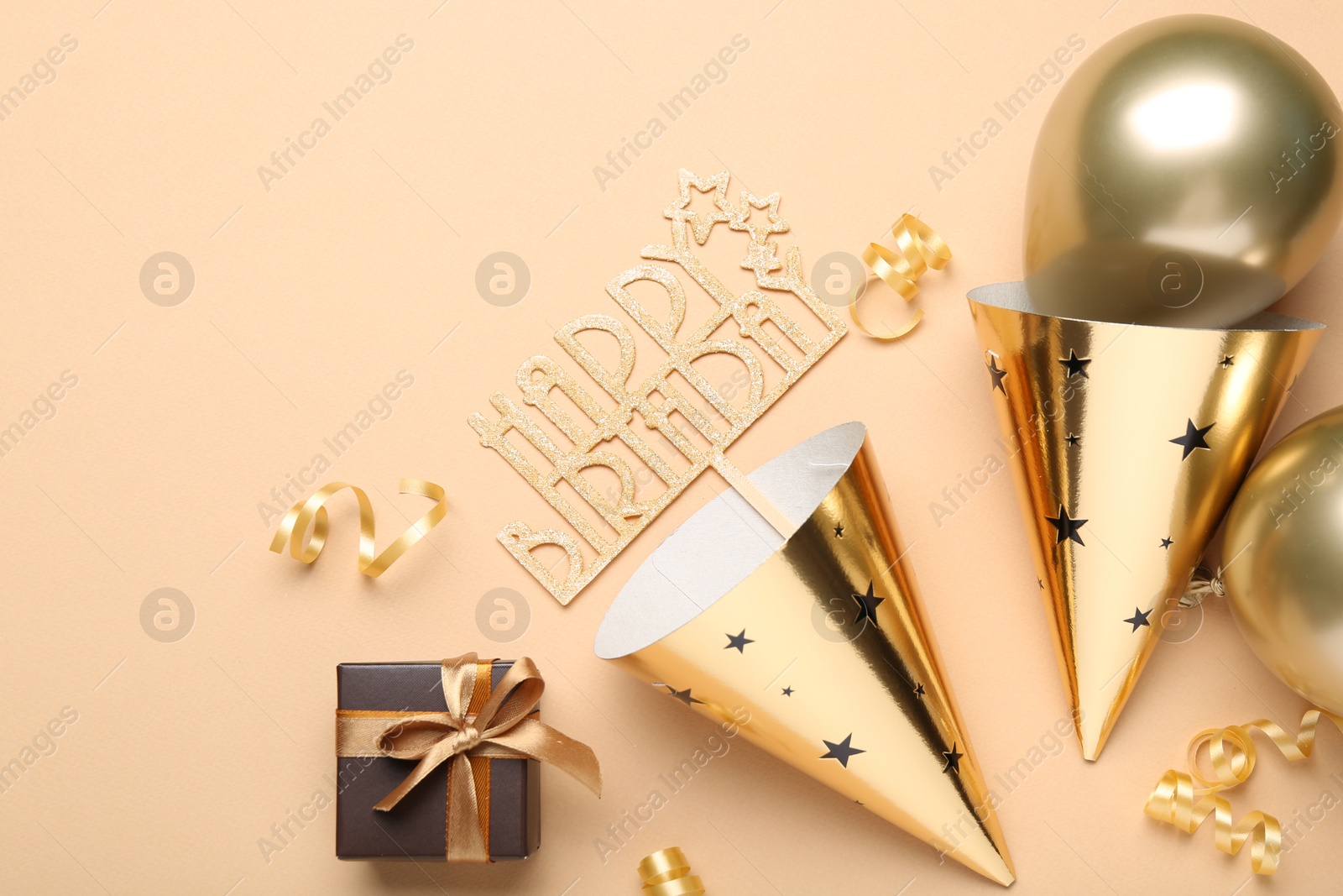 Party hats, topper, gift box and balloons on beige background, flat lay Photo of Party hats, topper, gift box and balloons on beige background, flat lay