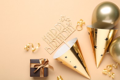 Photo of Party hats, topper, gift box and balloons on beige background, flat lay