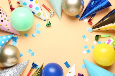 Photo of Frame of colorful party hats, balloons, blowers and confetti on beige background, flat lay. Space for text
