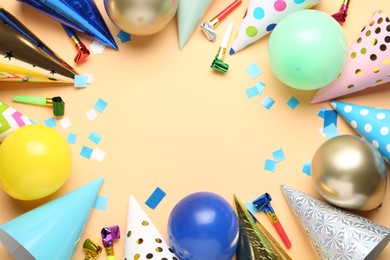 Photo of Frame of colorful party hats, balloons, blowers and confetti on beige background, flat lay. Space for text