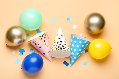 Photo of Colorful party hats, balloons and confetti on beige background, flat lay