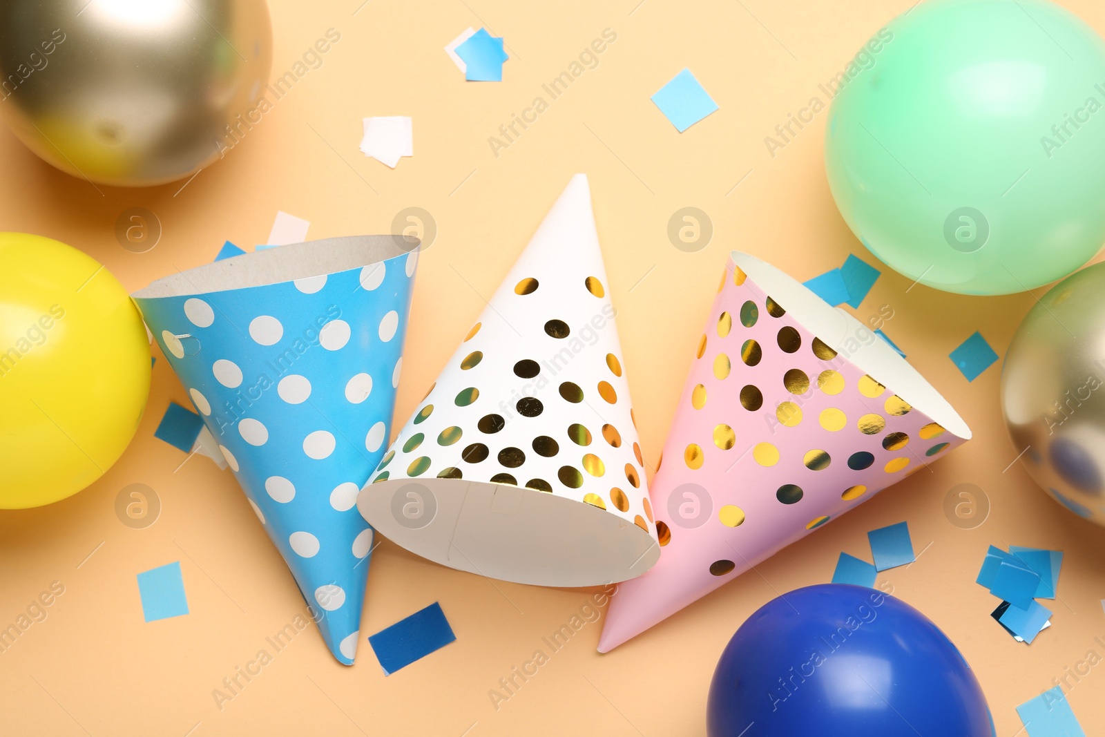 Colorful party hats, balloons and confetti on beige background, flat lay Photo of Colorful party hats, balloons and confetti on beige background, flat lay