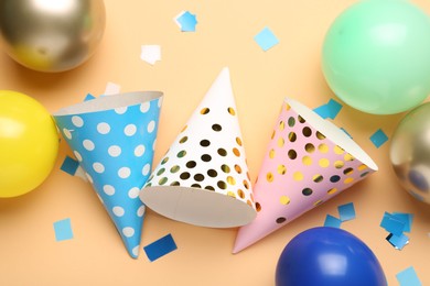Photo of Colorful party hats, balloons and confetti on beige background, flat lay