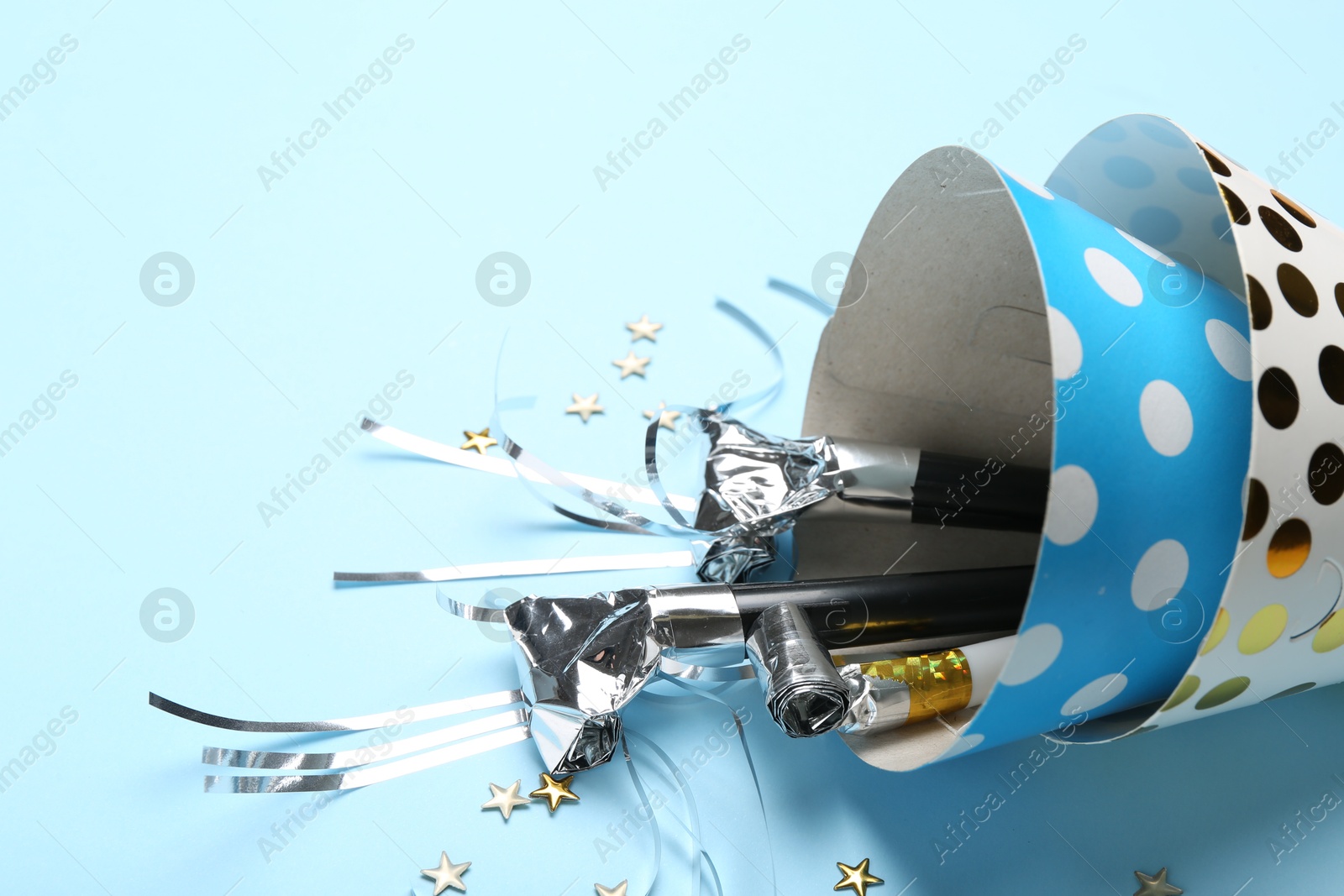 Party hats with blowers and confetti on light blue background, closeup. Space for text Photo of Party hats with blowers and confetti on light blue background, closeup. Space for text