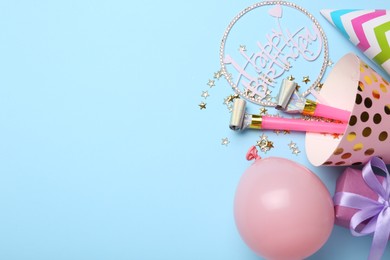 Photo of Party hats, topper, blowers, gift box and balloon on light blue background, flat lay. Space for text